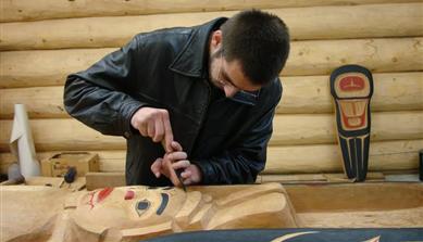 A man hand carving a totem pole